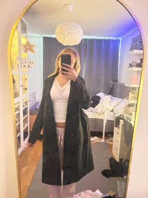 Svart lång kappa med klassisk krage - Säljer en svart lång kappa med klassisk krage och öppen front. Kappan har en rak passform och är tillverkad i ett mjukt tyg som ger en stilren look. Perfekt för dig som vill ha en enkel men snygg ytterjacka till hösten eller vintern.