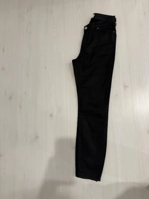 Svarta jeans från STOCKH LM - Säljer ett par svarta jeans från STOCKH LM med klassisk femficksmodell och raka ben. Jeansen har detaljer i guldmetall och är tillverkade i ett mjukt, stretchigt material som sitter snyggt. Perfekta för en stilren och enkel look.