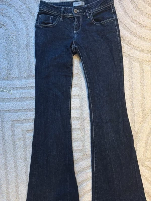 Mörkblå bootcut jeans - Säljer ett par mörkblå bootcut jeans med klassisk femficksdesign och kontrastsömmar. Jeansen har utsvängda ben och är tillverkade i ett mjukt denimtyg som sitter snyggt på kroppen. Perfekta för dig som gillar retrovibbar och vill ha en tidlös look.  Säljer dessa eftersom de är för korta för mig och jag är ungefär 167cm det är storlek 34 men känns som 32
