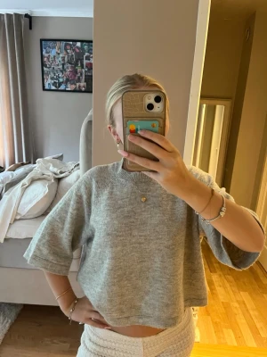 Stickad tröja ONLY - Säljer en ljusgrå croppad tröja med vida, halvlånga ärmar och rund halsringning. Tröjan har en avslappnad passform och är gjord i mjukt stickat material, perfekt för en chill och trendig look.
