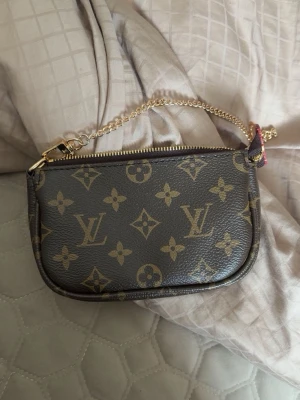 Brun väska - Snygg liten i klassiskt brunt . Väskan har guldfärgad kedja som handtag och dragkedja upptill. Perfekt för det viktigaste och ger en lyxig touch till din outfit.