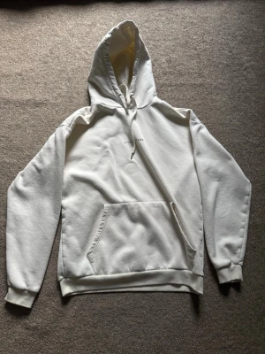 Vit hoodie från Icono Couture - Snygg vit hoodie från Icono Couture med tryck på ryggen och liten text framtill. Klassisk känguruficka, ribbade muddar och justerbar huva med dragsko. Perfekt för en clean och stilren look. Oversized.