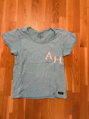 Ljusblå t-shirt med AH-tryck Adrian Hammond  - Ljusblå t-shirt med rund hals och korta ärmar. På bröstet finns ett vitt AH-tryck i tyg. T-shirten har en avslappnad passform och en liten svart etikett nertill. Perfekt för en chill och enkel stil. Adrian Hammond medium 
