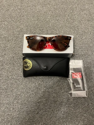 Leopardmönstrade Ray-Ban solglasögon - Säljer ett par snygga Ray-Ban solglasögon med leopardmönstrad båge och bruna glas. Klassisk fyrkantig form och levereras med originalfodral och putsduk. Perfekta för dig som vill sticka ut med en trendig accessoar.