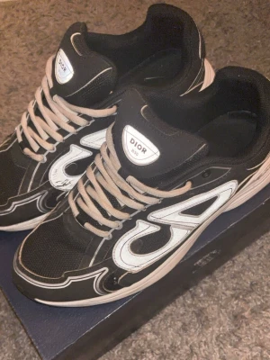 Svarta B30 sneakers med vit detalj - Snygga svarta B30 sneakers med vita och grå detaljer. Skorna har några skador men är fortfarande i bra skick. Priset kan diskuteras. Har också boxen kvar