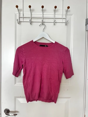 Rosa topp från 157 med kort ärm - En enkel och stilren rosa topp frånlager 157 med rund halsringning och korta ärmar. Toppen har en ribbad kant vid halsen och är tillverkad i ett mjukt material som känns skönt mot huden. Perfekt att matcha med jeans eller kjol.