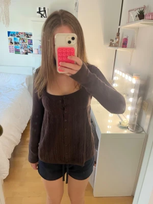 Stickad babydoll tröja  - Säljer en super mysig brun babydoll tröja med kabelstickat mönster och knappar hela vägen framtill från Hollister. Tröjan har lång ärm och fyrkantig urringning. 