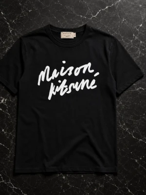 Svart Maison Kitsuné t-shirt - Snygg svart t-shirt från Maison Kitsuné med vit logotyp i handskriven stil på bröstet. Klassisk rund hals och korta ärmar. Tillverkad i mjuk bomull som känns skön mot huden. Perfekt för en clean och trendig look.