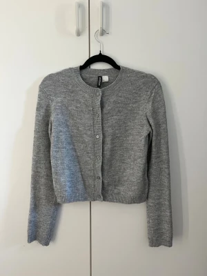 Grå kofta med knappar - Mysig grå kofta med rund hals och långa ärmar. Perfekt att slänga över en topp för en chill look. Koftan är använd några gånger men fortfarande i bra skick och passar till allt. En kofta från H&M i storlek S men passar även personer med XS. 