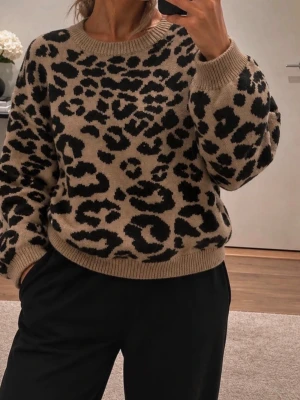 Leopardmönstrad stickad tröja AX Paris  - Stickad tröja från AX Paris i beige med svart leopardmönster. Tröjan har rund halsringning, ribbade muddar och en avslappnad passform. Perfekt för dig som vill ha en trendig och bekväm look med lite edge.