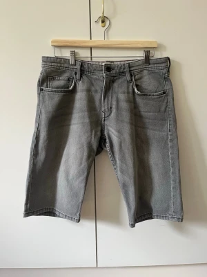 Grå jeansshorts från Esprit strl 31 - Säljer ett par grå jeansshorts från Esprit med klassisk femficksdesign och knappgylf. Shortsen har raka ben och normal passform. Material 99% bomull, 1% elastan. Storlek 31.