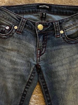 Jeans från true religion  - Blåa jeans från true religion i storlek 23. Använda ett par gånger därav slitage där nere vid fötterna och ett litet hål vid knät💕