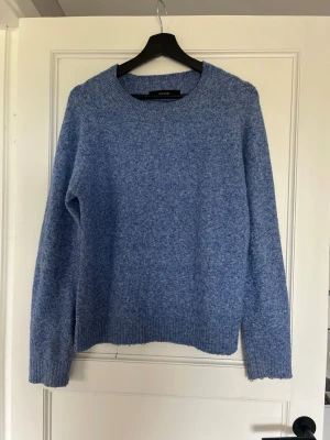 Blå stickad tröja från Vero Moda - Mysig blåmelerad stickad tröja från Vero Moda med rund halsringning och långa ärmar. Tröjan har en enkel, rak passform och ribbstickade muddar vid ärmslut och nederkant. Perfekt för lager på lager och chill dagar.