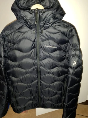 Mörkblå dunjacka från Peak Performance - Snygg mörkblå dunjacka från Peak Performance med quiltad design och dragkedja framtill. Jackan har huva och logga på bröstet. Perfekt för kalla dagar när du vill hålla värmen och ändå se stilren ut. Helt ny oanvänd nypris 2999 säljes för 1500 äkta som sagt tio av tio oanvänd. Passar smal o medium ned nypris 3400 nya modellen 
