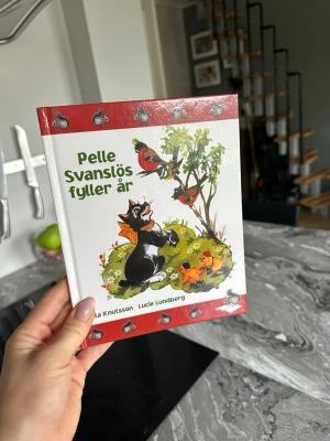 Pelle Svanslös fyller år bok - En färgglad bilderbok med hårda pärmar, illustrerad med Pelle Svanslös och andra djur. Boken har röd och vit framsida med tecknade figurer och är skriven av Gösta Knutsson och Lucie Lundberg. Perfekt för dig som gillar klassiska barnböcker.