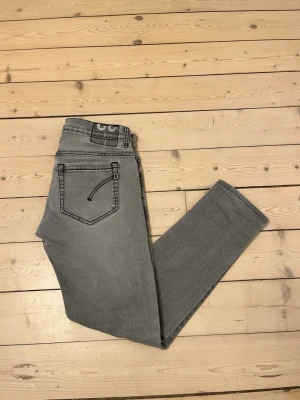 Grå Dondup George jeans  - Snygga ljusgrå Dondup jeans i modellen George med slim fit-passform och klassisk femfickssdesign. De är storlek W30 men de sitter mer som W29. Byxorna har svarta detaljer och diskret Dondup-logga samt raka ben. Jeansen är i mycket bra skick utan hål eller defekter. Nypris ca 3000kr.