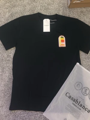 Svart t-shirt från Casablanca - Säljer en svart t-shirt från Casablanca med ett färgglatt tryck på bröstet i orange, gul och grön. T-shirten har klassisk passform och rund hals. Fraktar samma dag