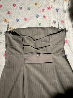 Grå kort bandeau klänning - Snygg grå bandeau-klänning med diskreta vertikala ränder. Klänningen har en unik detalj i ryggen med dekorativa band. Figurnära passform och stilren look, perfekt för dig som gillar minimalistisk stil.
