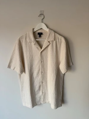 Kortärmad skjorta från H&M - Beige med korta ärmar och knappar framtill. Vågigt mönster. Lite konstigt sydd på ett ställe på ryggen men inget som syns på långt håll.