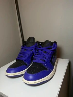 Air Jordan 1 Mid Dark Concord - Säljer ett par Nike Air Jordan 1 Mid i färgen Black/Dark Concord. En stilren svart/lila colorway med vita mellansulor som passar till de flesta outfits. Skorna är använda men i fint skick med normalt slitage, se bilder för skick. Bekväma och populära sneakers från Jordan Brand. Hör gärna av dig vid frågor eller om du vill ha fler bilder. Kartong medföljer ej.