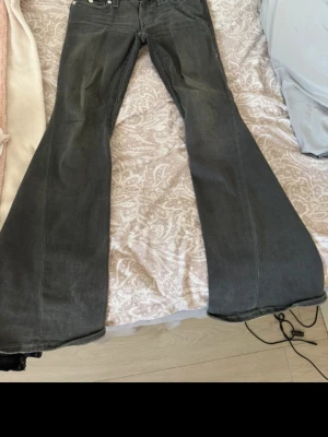 Gråa utsvängda jeans - Säljer ett par gråa jeans med riktigt breda utsvängda ben. Klassisk femficksmodell med snygga detaljer på bakfickorna. Jeansen har hög midja och är tillverkade i ett mjukt denimtyg som sitter skönt. Perfekta för dig som gillar retrostil och vill sticka ut.