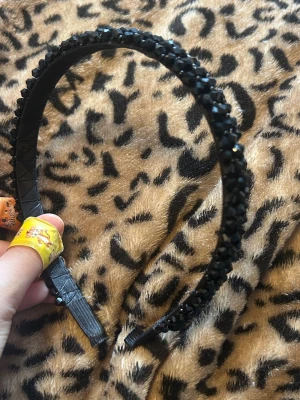 Svart diadem med glittrande stenar - Snyggt svart diadem dekorerat med glittrande svarta stenar som ger en lyxig känsla. Diademet har en klassisk form och är tillverkat i plast med stenar som sitter tätt längs hela bandet. Perfekt accessoar för att lyfta din look.