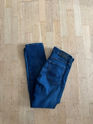 Jack&jones slim fit glenn - Snygga mörkblå jeans i slim fit-modell med klassisk femficksdesign och svarta detaljer vid linningen. Jeansen har en smal passform och är tillverkade i ett mjukt denimtyg som ger en skön känsla. Perfekta för dig som gillar en stilren och enkel look.