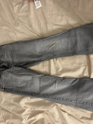 Grå bootcut jeans - Säljer ett par gråa bootcut jeans med klassisk femficksmodell och normal midja. Jeansen har en snygg tvättad look och är tillverkade i ett mjukt denimtyg som ger en avslappnad vibe. Perfekta för dig som gillar en lite vidare passform nedtill.