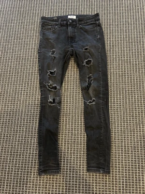 Svarta ripped jeans Only & Sons - Säljer ett par svarta skinny jeans från Only & Sons med flera slitningar och hål på framsidan. Jeansen har klassisk femficksmodell och knappgylf. Materialet är stretchigt för en bekväm passform och de har en trendig, sliten look.