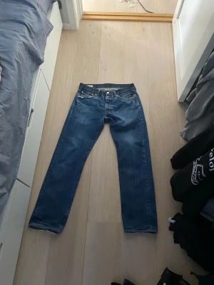 Blå raka jeans med slitna detaljer - Säljer ett par klassiska blå jeans med raka ben och slitna detaljer vid fickorna. Jeansen har fem fickor, bälteshällor och stängs med knapp och dragkedja. Perfekta för en avslappnad och cool stil.