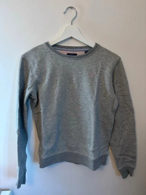 Grå sweatshirt från GANT - En enkel och stilren grå sweatshirt med rund halsringning och ribbade muddar vid ärmslut och nederkant. Tröjan har en liten diskret logga broderad på bröstet och är tillverkad i mjukt sweatshirtmaterial. Perfekt för en avslappnad look.