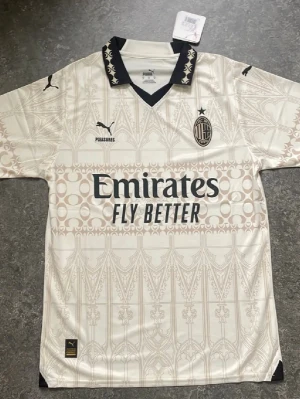 AC Milan vit matchtröja Puma - Snygg vit AC Milan matchtröja från Puma med svart krage och detaljer. Tröjan har mönstrad design, klubbmärke och sponsorloggor på bröstet samt tryck på ryggen. Perfekt för fotbollsfans som vill sticka ut på läktaren eller planen. Är öppen för prisförslag.