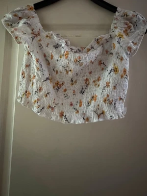 Vit blommig croppad topp - Söt vit croppad topp med blommigt mönster i gult och orange. Toppen har korta puffärmar, volangdetaljer vid ärmslutet. Har använt den cirka 2 gånger 
