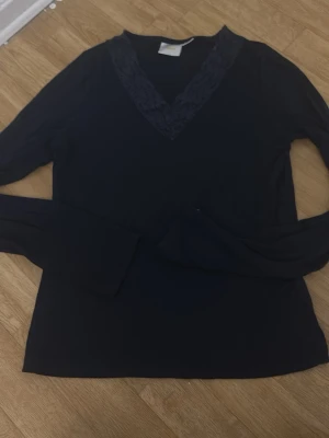 Mörkblå långärmad topp Gina Tricot - Mörkblå långärmad topp från Gina Tricot med v-ringning och spetsdetaljer runt halsen. Perfekt att styla med jeans eller kjol för en snygg och enkel look.