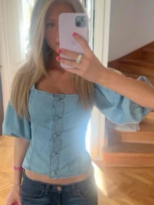 Ljusblå puffärmad korsettopp - Trendig ljusblå korsettopp i denim-look med puffärmar och knappar framtill. Använd fåtal gånger. Från H&M i storlek xs. 