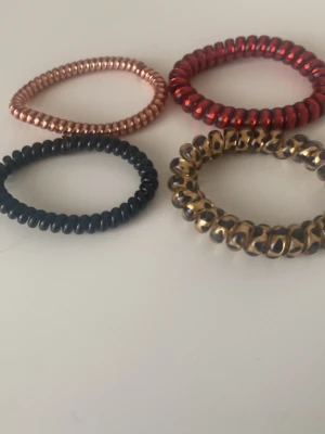 Spiralsnoddar i olika färger - Fyra spiralsnoddar i plast, perfekta för att sätta upp håret utan att det trasslar. Färgerna är svart, guld med svart, metallic röd och koppar. Snygga accessoarer som ger en cool touch till din look.
