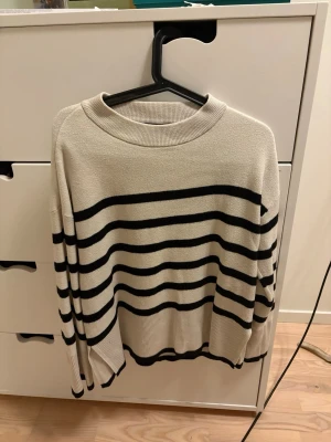 Beige stickad tröja med svarta ränder - Snygg stickad tröja från Vero Moda. Har en liten fläck vid armbågen som knappt syns när man har på sig den.