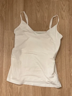 Vit enkel linnetopp - Säljer en vit linnetopp med smala axelband och v-ringad hals. Toppen är ärmlös och har en clean, basic look som passar till det mesta. Perfekt att styla lager på lager eller bära som den är under varma dagar.