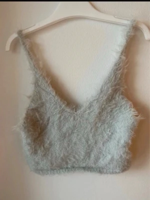 Ljusgrå fluffig linnetopp - Supermjuk och fluffig ljusgrå linnetopp med v-ringning och smala axelband. Perfekt för dig som vill ha en mysig och trendig topp till din outfit. Materialet är syntetiskt med en pälsliknande känsla.