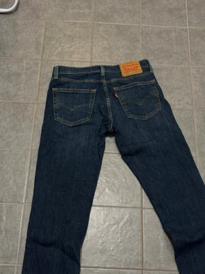 Levi's 511 mörkblå jeans W30 L34 - Säljer ett par klassiska Levi's 511 jeans i mörkblå denim med raka ben och snygga kontrastsömmar. Jeansen har två bakfickor med den ikoniska Levi's-sömmen och läderpatch bak i midjan. Perfekta för en avslappnad och stilren look.