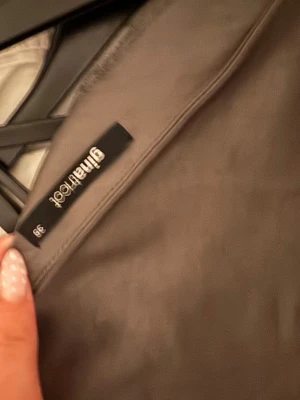 Mörkgrå satinblus Gina Tricot - Snygg mörkgrå satinblus från Gina Tricot i storlek 38. Blusen har lång ärm och en rak, något kortare passform. Materialet är glansigt och ger en lyxig känsla. Perfekt att styla med höga jeans eller kjol.