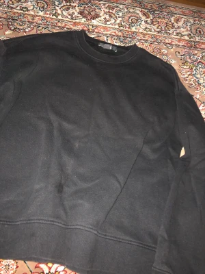 Svart sweatshirt från Primark - En enkel svart sweatshirt från Primark i storlek L. Tröjan har rund halsringning, långa ärmar och ribbade muddar vid ärmslut och nederkant. Perfekt basplagg till garderoben och lätt att matcha med olika stilar.
