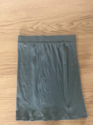 Grön ribbad kortkjol - Säljer en enkel och stilren grön kortkjol med ribbad struktur. Kjolen har en bred resår i midjan och är gjord i ett mjukt, stretchigt material som sitter snyggt på kroppen. Perfekt att matcha med en crop top eller hoodie.