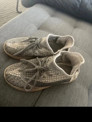 Gråmönstrade stickade sneakers - Säljer ett par grå och beige sneakers med stickad ovandel och mönstrade skosnören. Skorna har en låg profil och en bekväm, flexibel sula. Perfekta för dig som gillar en modern och avslappnad stil.