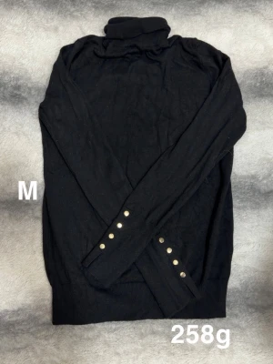 Svart polotröja med gulddetaljer - Stilren svart polotröja med långa ärmar och snygga guldfärgade knappar vid ärmsluten. Tröjan har ribbade muddar, perfekt till lager på lager. Enkel att matcha med olika outfits.🌸 Fint använt skick. Storlek M