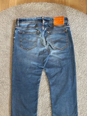 Jacob cohen 688 - Säljer ett par Jacob Cohens i midja 32 och längd på 97 vilket motsvarar längd 30 på jeans cirka. Dem är i bra skick med lite wear and tear på lappen där bak men annars har dem inga skavanker! Passform är regular/straight 