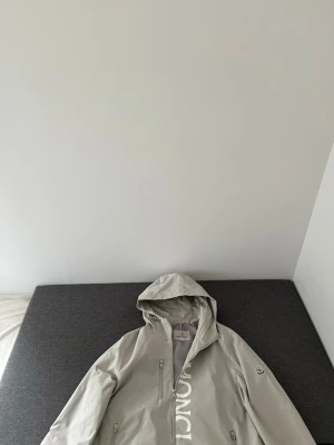 Ljusgrå vindjacka från Moncler - Snygg ljusgrå vindjacka från Moncler med huva och dragkedja framtill. Jackan har två sidofickor med dragkedja och Moncler-logga på ärmen. Tillverkad i ett lätt och vindtätt material, perfekt för blåsiga dagar. Aldrig använd enbart testad 