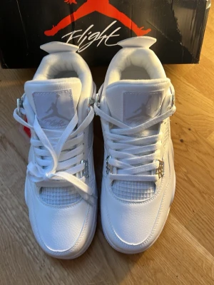 Vita höga sneakers med silvriga detaljer - Säljer ett par helvita höga sneakers från Jordan med silvriga detaljer vid snörningen och klassisk mesh på sidan. Skorna har en chunky sula och ikonisk Jumpman-logga på plösen. Tillverkade i läder och mesh för en clean och sportig look.