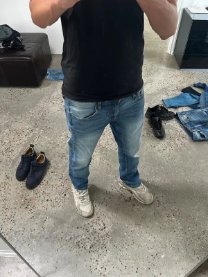 Ljusblå raka jeans herr - Säljer ett par ljusblå jeans med rak passform och klassisk femficksdesign. Jeansen har slitningar och tvättade detaljer för en avslappnad look. Perfekta till sneakers och t-shirt för en chill stil.