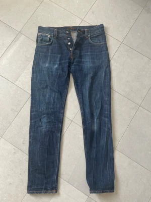 Seldvedge jeans från Nudie  - Säljer ett par klassiska mörkblå seldvedge jeans från Nudie Jeans med raka ben och knappgylf. Fina slitningar som börjar synas på fickan och även vid knäna. Knappt använda och i toppskick. De har dock krympt aningen i midjan i tvätten  men  passar forf mig som brukar bära 30/32. Tveka inte att ställa frågor☺️